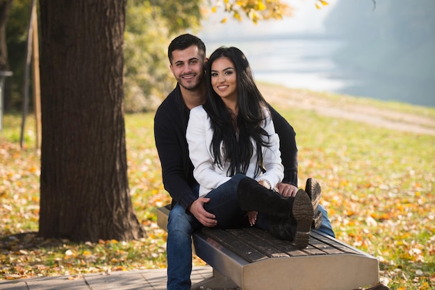 Pareja joven sentada en un banco en el hermoso día de otoño