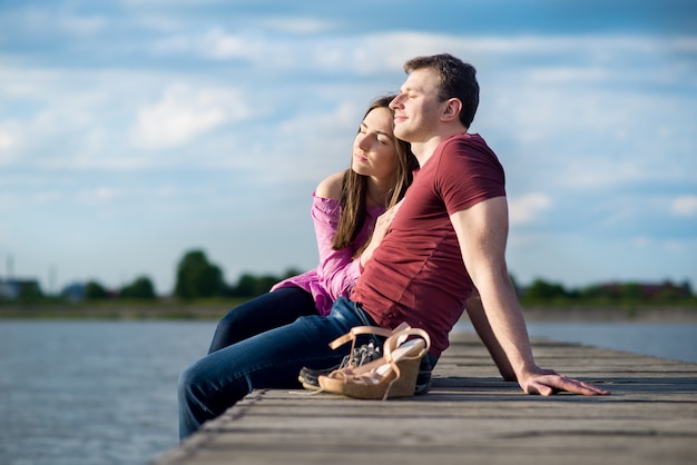 Pareja joven sentada en bridga de madera en el lago