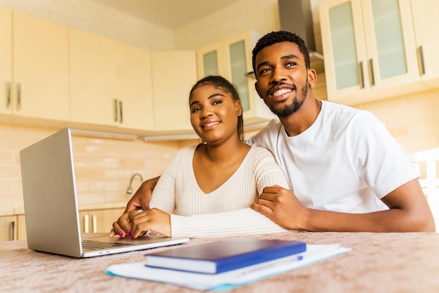 Pareja joven sentada con una computadora portátil y educación en línea en la cocina en casa