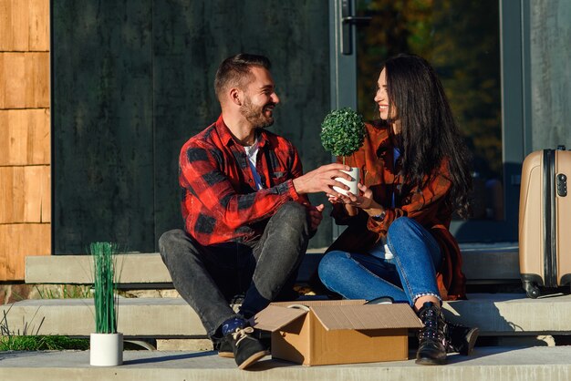 Foto pareja joven sentada en las escaleras divirtiéndose desembalaje de cajas después de mudarse a casa nueva.