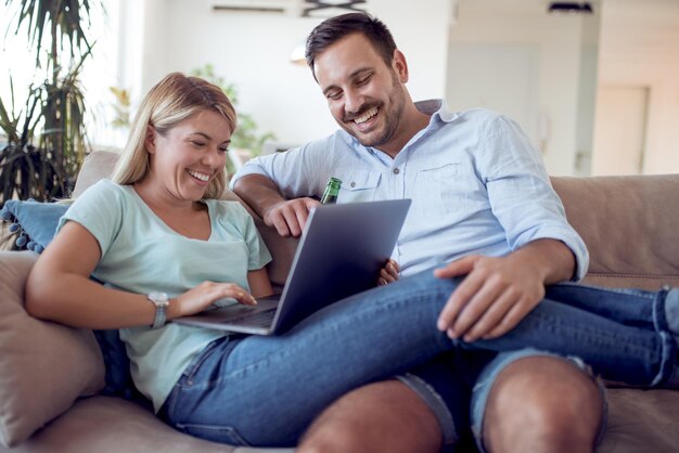 Una pareja joven sentada en la sala de estar y usando una laptop