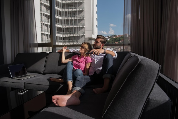 Foto una pareja joven sentada en un sofá cerca de la ventana viendo la televisión juntos en una casa de lujo