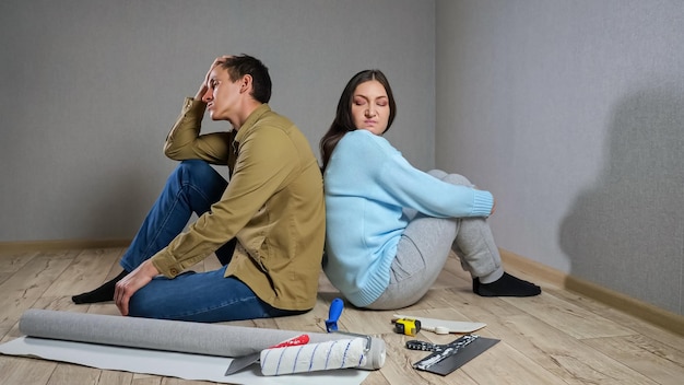 Pareja joven se sienta en el piso de parquet entre materiales de construcción en la habitación después de la pelea debido a las renovaciones.