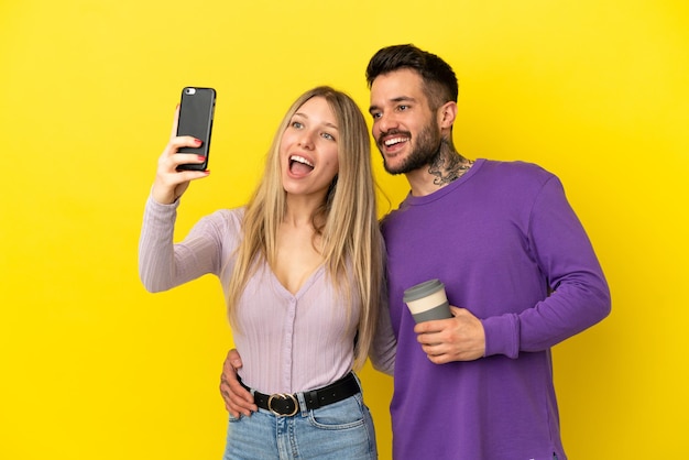 Pareja joven sobre fondo amarillo aislado haciendo un selfie con el móvil