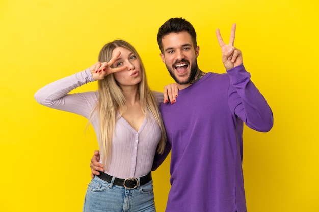 Pareja joven sobre fondo amarillo aislado sonriendo y mostrando el signo de la victoria