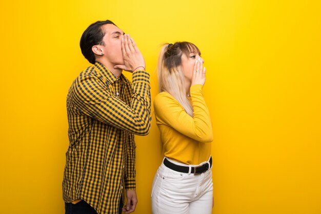 Pareja joven sobre fondo amarillo vibrante gritando con la boca abierta