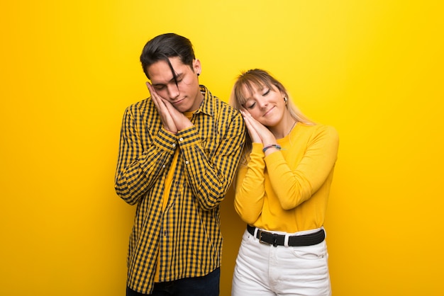 Foto pareja joven sobre fondo amarillo vibrante haciendo gesto de sueño