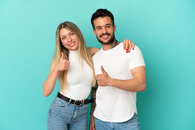 Foto pareja joven sobre fondo azul aislado dando thumbs up gesto