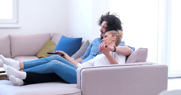 Pareja joven en el sofá viendo la televisión juntos en su casa de lujo