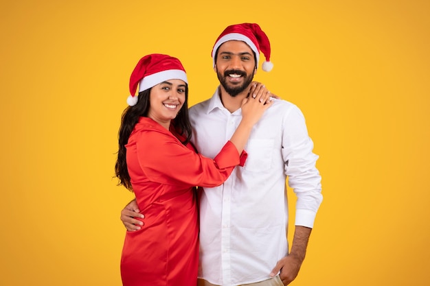 Pareja joven con sombreros de Navidad abrazándose sobre fondo amarillo