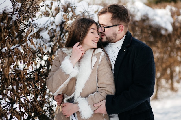 Pareja joven sonríe y besándose en el parque en invierno