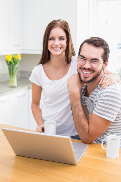 Pareja joven sonriendo a la cámara usando la computadora portátil