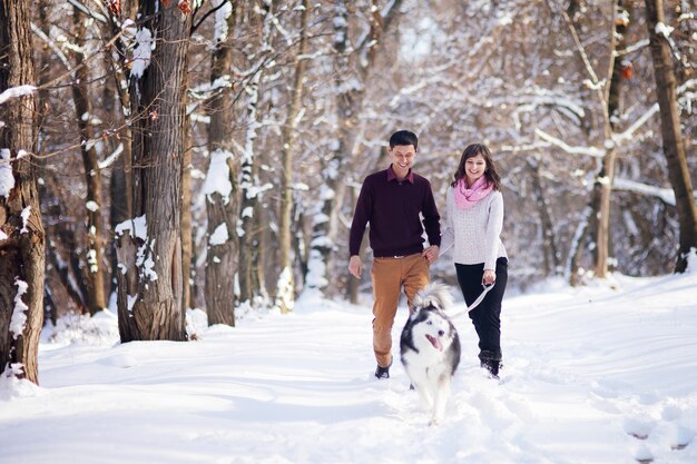 Pareja joven sonriendo y divirtiéndose en Winter Park con su perro husky.