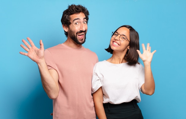 Pareja joven sonriendo feliz y alegremente, saludando con la mano, dándote la bienvenida y saludándote, o despidiéndose