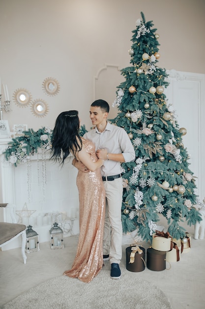 Pareja joven sonriendo mientras celebra en casa cerca de un árbol de Navidad