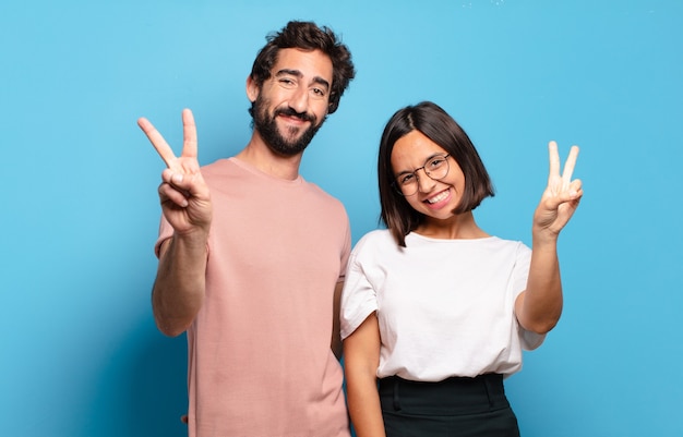 Pareja joven sonriendo y mirando amigable, mostrando el número dos o el segundo con la mano hacia adelante, contando hacia atrás