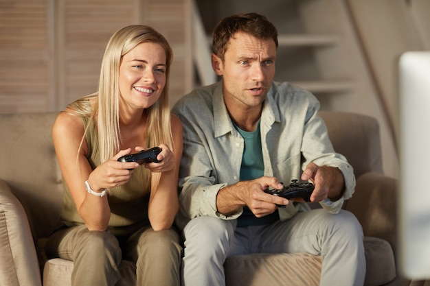 Pareja joven sonriente divirtiéndose mientras juega en el juego de computadora en casa