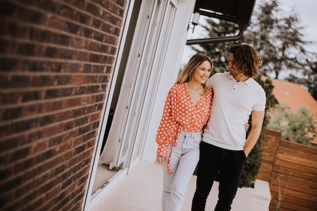 Pareja joven sonriente enamorada caminando frente a la pared de ladrillo de la casa