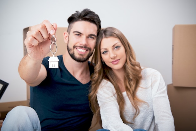 Foto pareja joven sonriente sosteniendo sus nuevas llaves de la casa, concepto de bienes raíces y reubicación