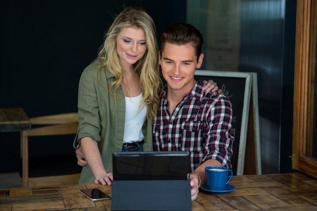 Pareja joven sonriente con tablet PC en la mesa en la cafetería.