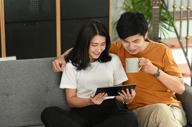 Pareja joven sonriente con tableta digital mientras está sentado en el sofá en casa.