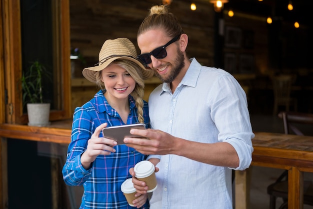 Pareja joven sonriente con teléfonos inteligentes en la cafetería.