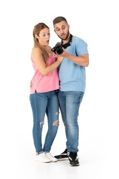 Foto pareja joven sorprendida mirando fotos en su cámara con un fondo blanco perfecto visten ropa casual jeans y camisas azul y rosa