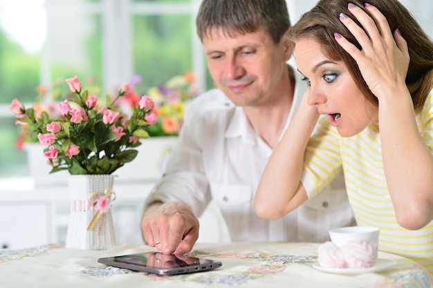 Pareja joven sorprendida sentada en la mesa y mirando la tableta digital