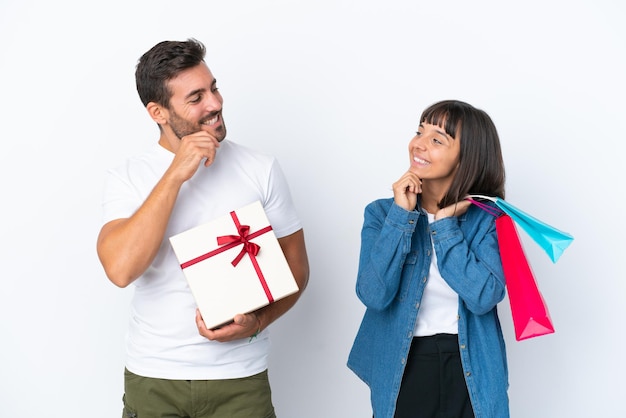 Pareja joven sosteniendo bolsas de la compra y presente aislado sobre fondo blanco mirando el uno al otro