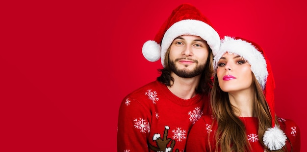 Pareja joven en suéteres de navidad y sombreros de santa feliz celebración de año nuevo felices fiestas