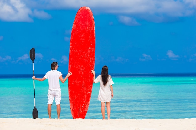 Pareja joven con tabla de surf roja durante vacaciones tropicales