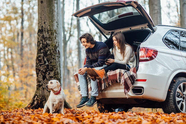 Pareja joven tiene un picnic con su perro cerca del automóvil en el bosque.