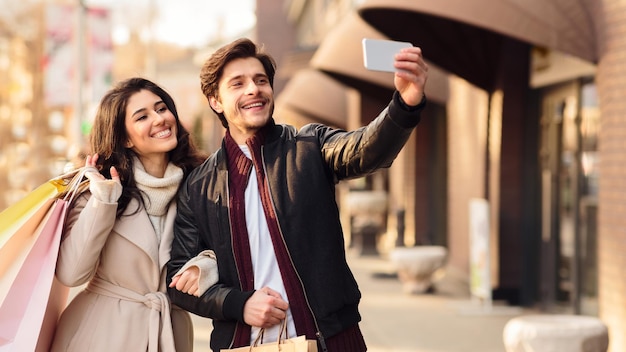 Pareja joven tomando selfie cerca de boutiques al aire libre