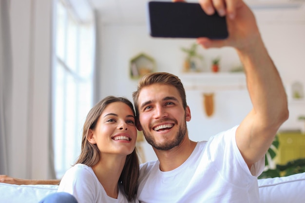 Pareja joven tomando un selfie en el sofá en casa en la sala de estar