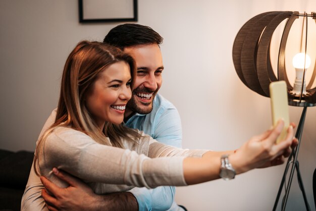 Foto pareja joven tomando selfies con su teléfono inteligente en su casa.