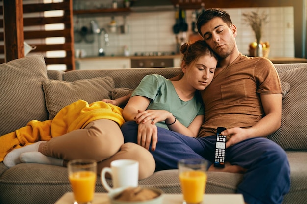 Pareja joven tomando una siesta en el sofá mientras ve la televisión en casa