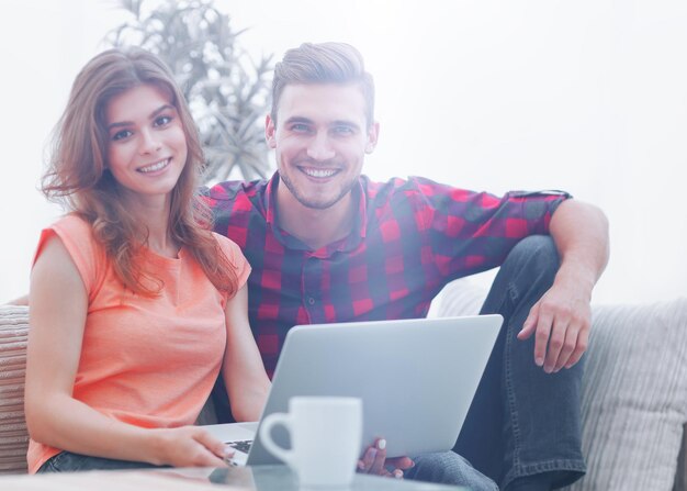 Una pareja joven trabajando en una laptop sentada en un sofá frente a una mesa de café