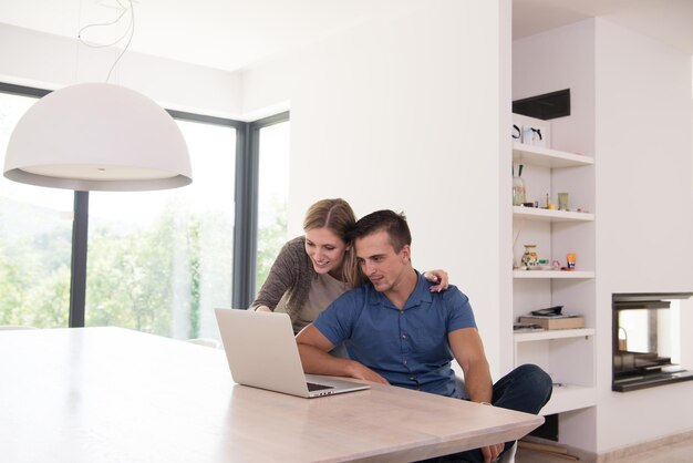 Pareja joven usando computadora portátil en casa de lujo juntos, mirando la pantalla, sonriendo.