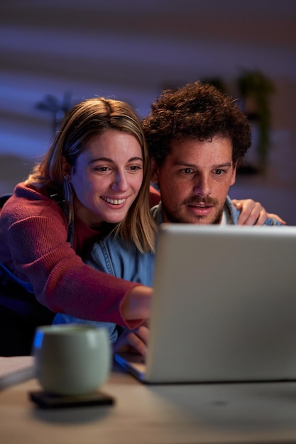 Una pareja joven usando una computadora portátil juntos en casa durante la noche buscando un destino de viaje