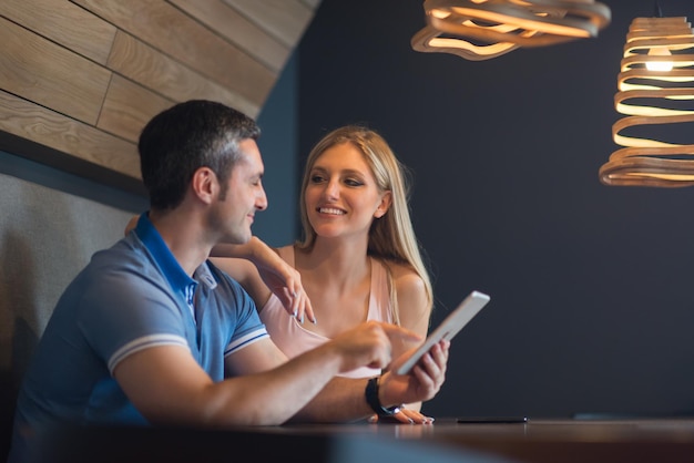 Una pareja joven usando una tableta en una casa de lujo juntos, mirando la pantalla, sonriendo.