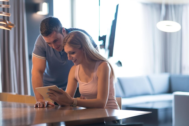 Una pareja joven usando una tableta en una casa de lujo juntos, mirando la pantalla, sonriendo.