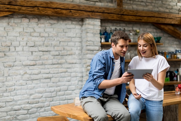 Pareja joven usando una tableta digital y sonriendo mientras está sentado en la mesa en casa