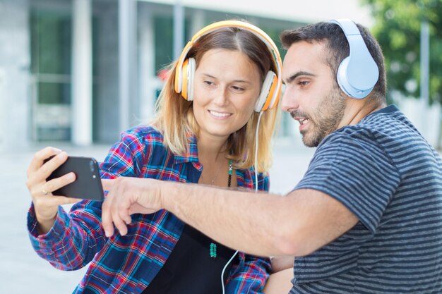 Foto una pareja joven usando el teléfono mientras escucha música en la ciudad