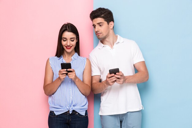 Pareja joven usando teléfonos inteligentes juntos, aislado sobre pared colorida