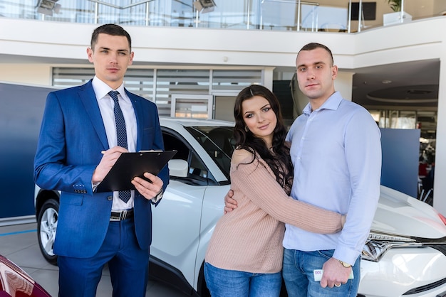 Pareja joven con vendedor cerca de contrato de firma de coche nuevo