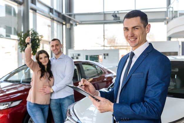 Pareja joven con vendedor cerca de contrato de firma de coche nuevo