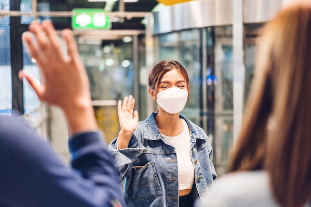 Pareja joven viajero en cuarentena por coronavirus con máscara quirúrgica protección facial saludando y saludando con un amigo después de un largo viaje de vacaciones en el aeropuerto de la terminal internacional