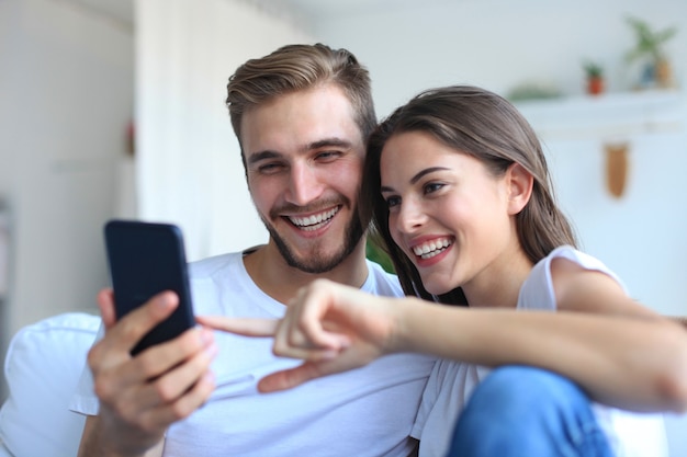 Pareja joven viendo contenido en línea en un teléfono inteligente sentado en un sofá en casa en la sala de estar