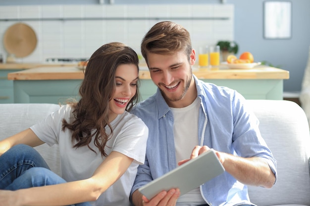 Pareja joven viendo contenido multimedia en línea en una tableta sentado en un sofá en la sala de estar.