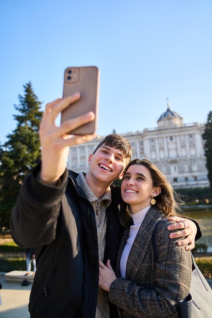 Pareja joven visitando el palacio real de Madrid haciéndose un selfie con sus smartphones